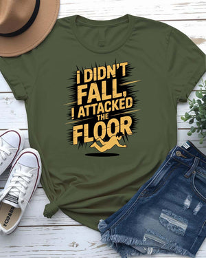 Funny unisex t-shirt that reads “I Didn’t Fall I Just Attacked The Floor” in bold meme font, modeled by man and woman in casual indoor setting.