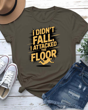 Funny unisex t-shirt that reads “I Didn’t Fall I Just Attacked The Floor” in bold meme font, modeled by man and woman in casual indoor setting.