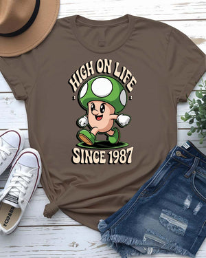 Retro meme T-shirt with High on Life Since 1987 text in vintage-style lettering, worn by a smiling model in natural light.