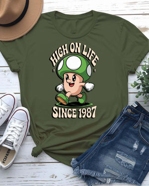 Retro meme T-shirt with High on Life Since 1987 text in vintage-style lettering, worn by a smiling model in natural light.