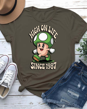 Retro meme T-shirt with High on Life Since 1987 text in vintage-style lettering, worn by a smiling model in natural light.