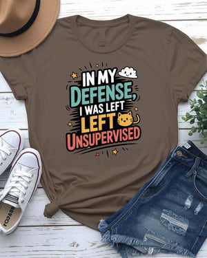 Unisex T-shirt with “In My Defense I Was Left Unsupervised” text in bold white distressed typography – worn by male and female models, casual setting.