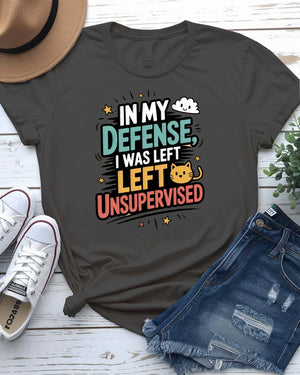 Unisex T-shirt with “In My Defense I Was Left Unsupervised” text in bold white distressed typography – worn by male and female models, casual setting.