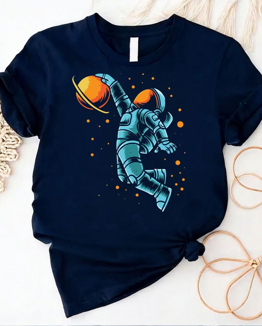 Astronaut playing basketball on moon surface graphic tee