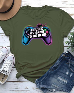 Unisex tee with bold “Paused My Game to Be Here” text in pixel-style typography, modeled by gamer in headset and controller.