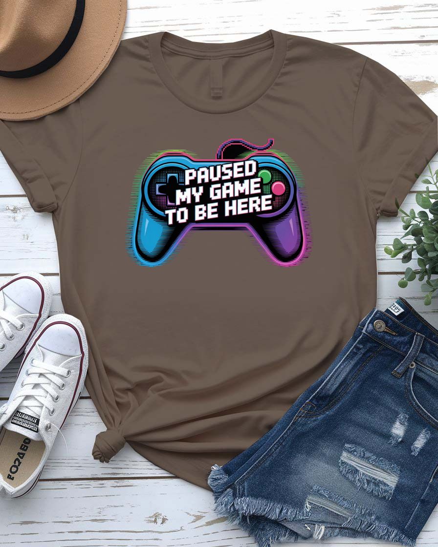 Unisex tee with bold “Paused My Game to Be Here” text in pixel-style typography, modeled by gamer in headset and controller.