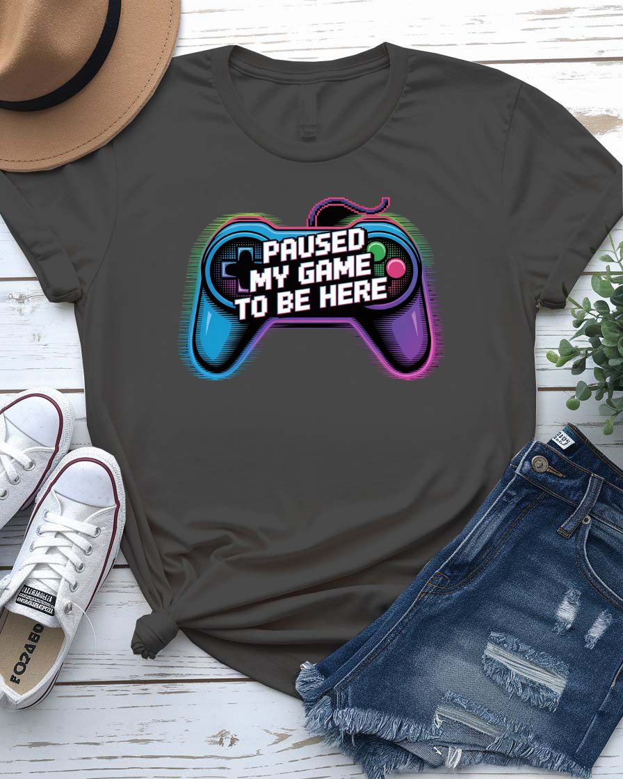 Unisex tee with bold “Paused My Game to Be Here” text in pixel-style typography, modeled by gamer in headset and controller.